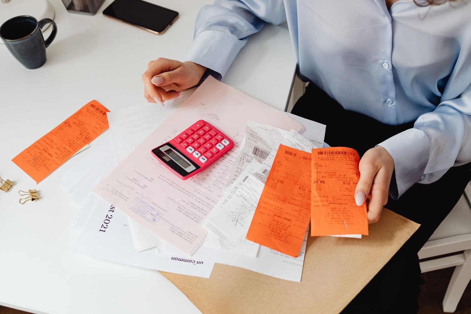 A shoebox of paper receipts being sorted with a calculator and phone