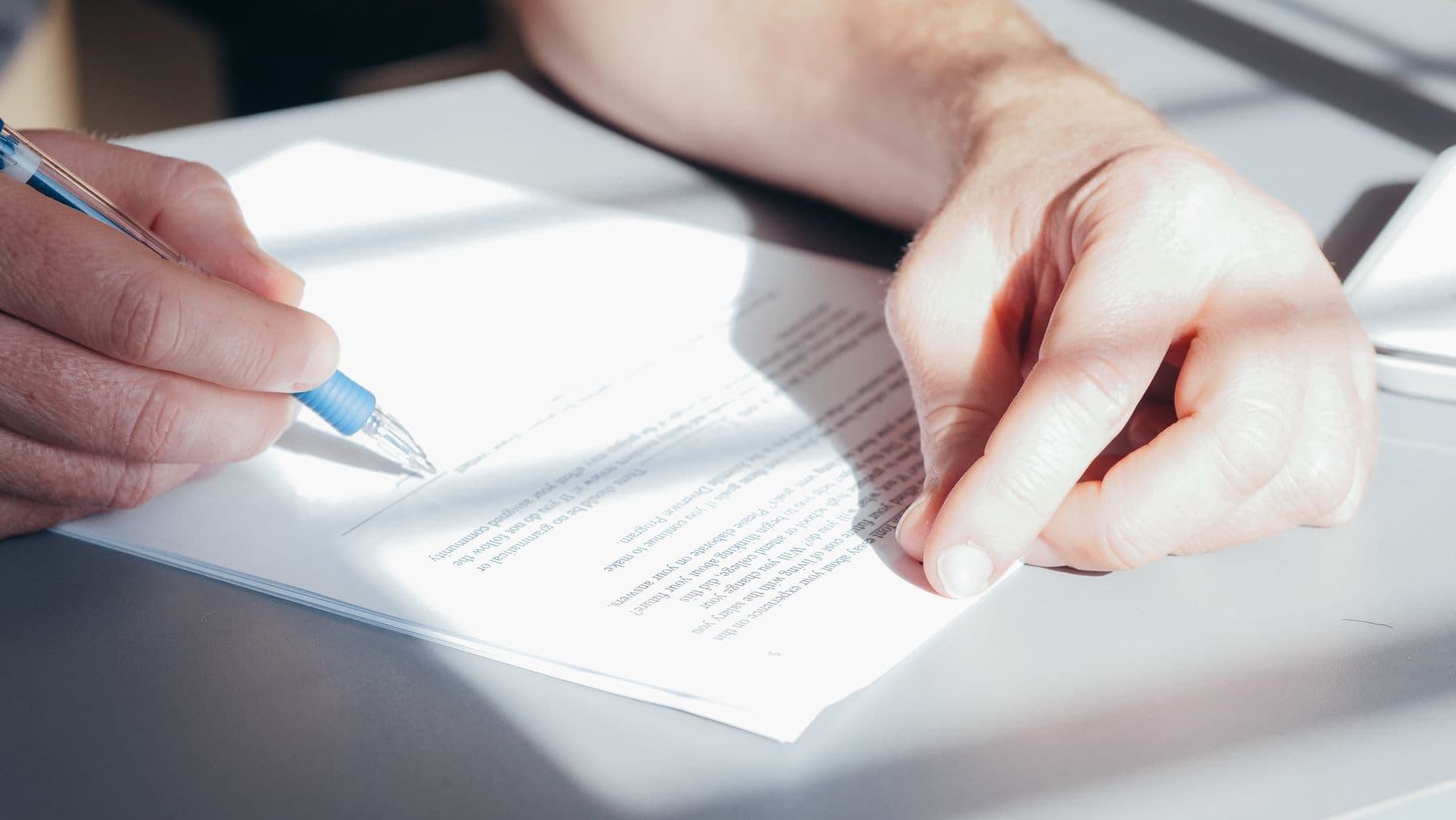 Two people signing a contract across a desk